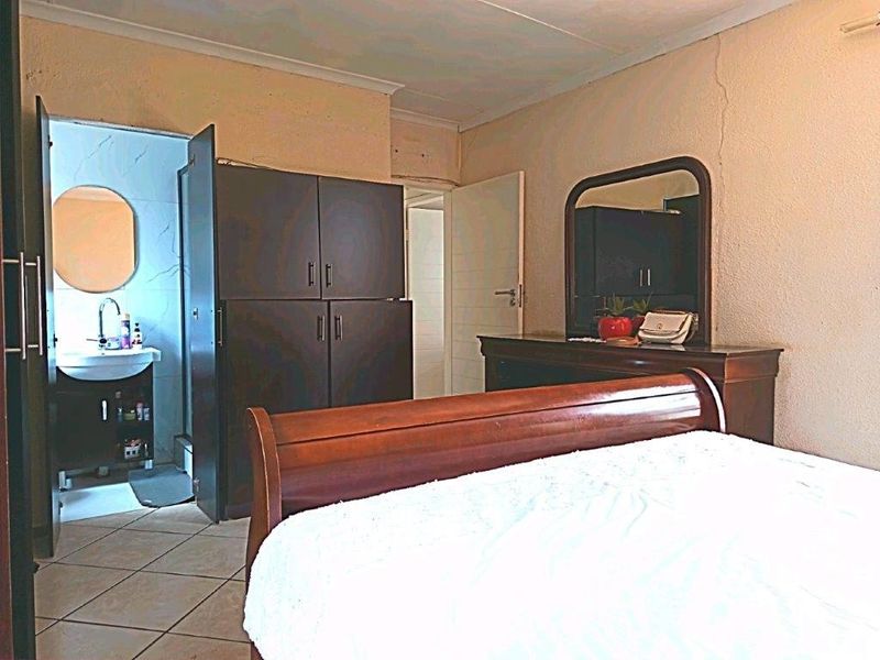 Bedroom featuring tiled flooring and an attached en-suite bathroom, showing signs of wear including visible wall cracks.