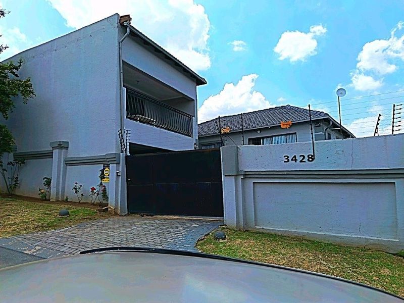 Front view of a two-story residential property featuring a paved driveway, secure perimeter wall with electric fencing, and a balcony.