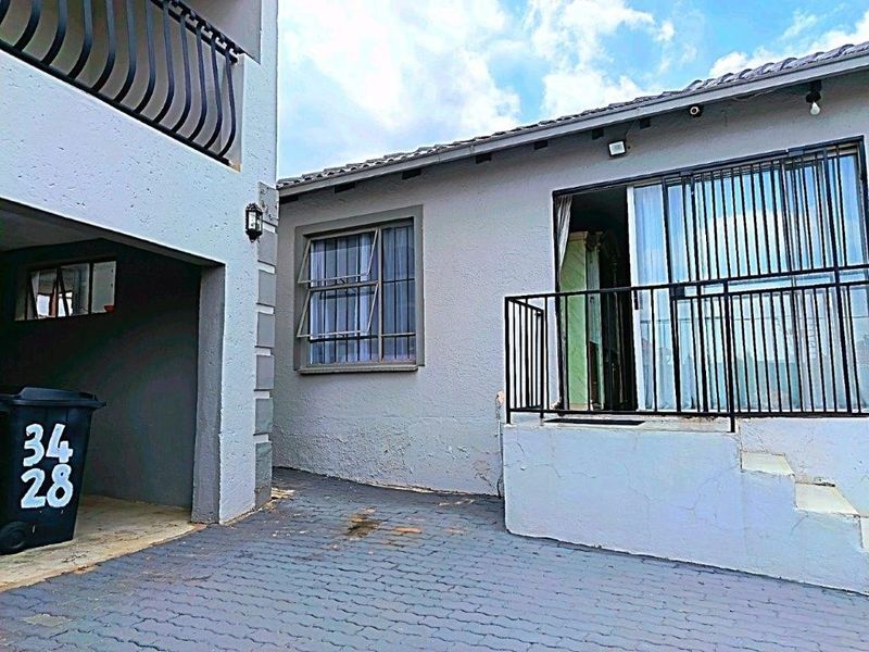 Rear exterior view showing a paved courtyard area, sliding door access with security gate, and balcony above.