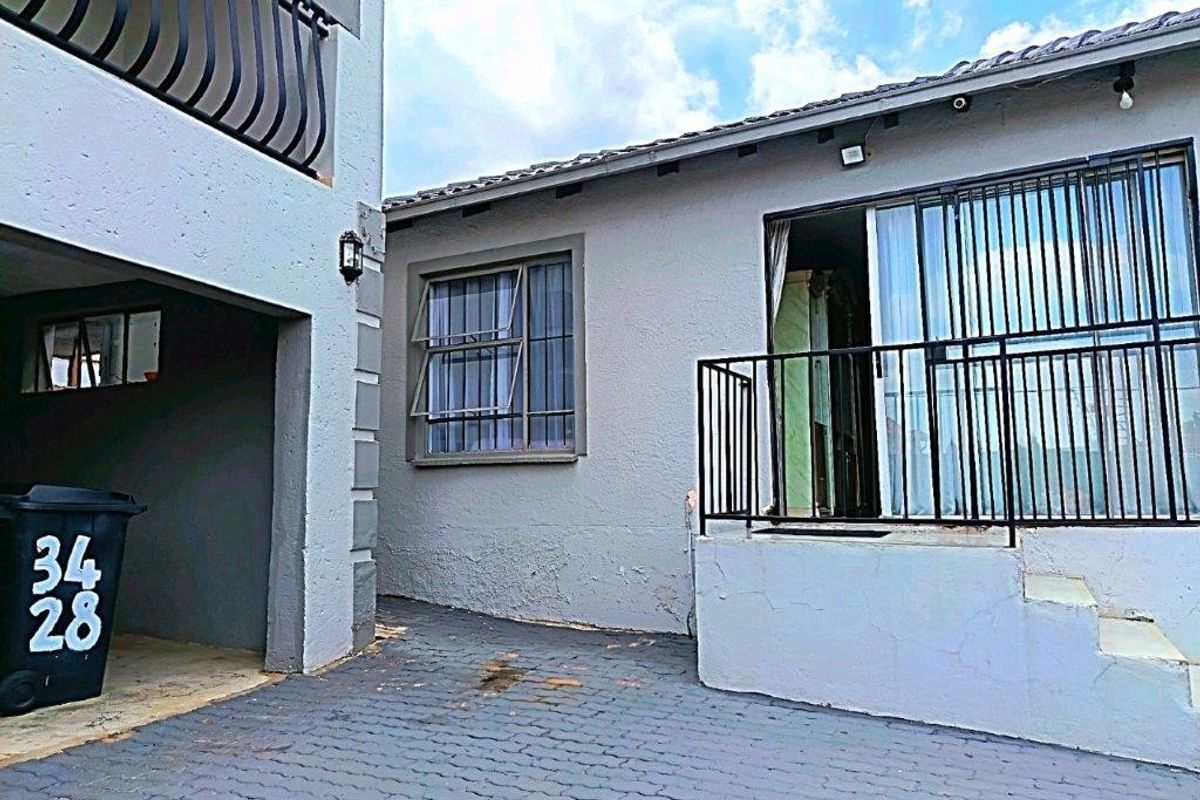 Rear exterior view showing a paved courtyard area, sliding door access with security gate, and balcony above.