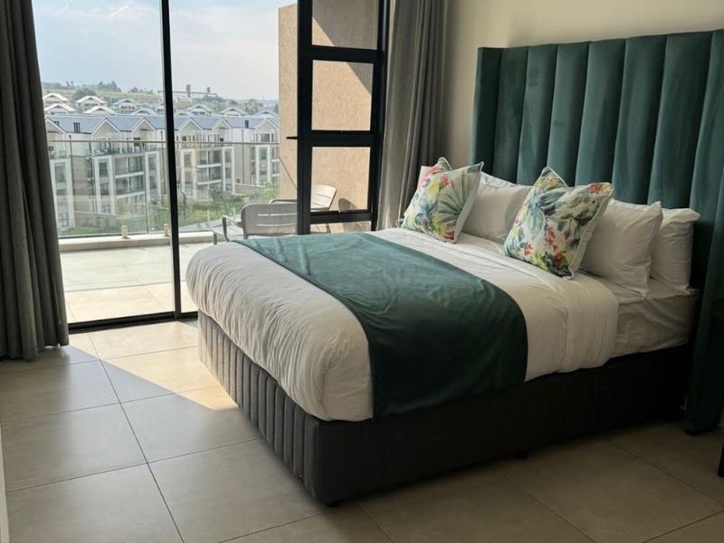 Modern bedroom featuring large format floor tiles and a large sliding glass door providing access to a private balcony with neighborhood views.