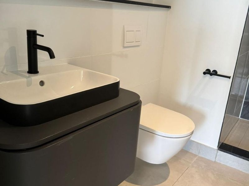 Modern bathroom featuring a wall-mounted vanity with a vessel sink, black fixtures, and a wall-hung toilet with a concealed cistern.