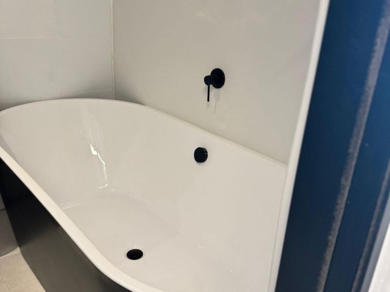 A modern bathroom featuring a sleek black and white freestanding bathtub with minimalist wall-mounted matte black fixtures.