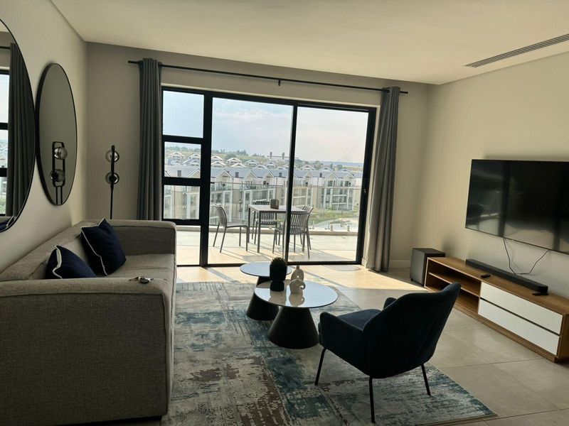 Modern living room featuring large sliding glass doors that open onto a balcony with expansive estate views and neutral tiled flooring.