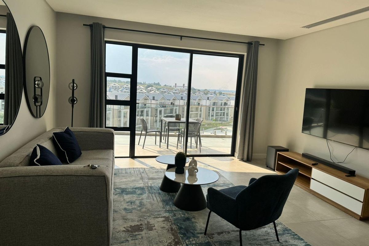 Modern living room featuring large sliding glass doors that open onto a balcony with expansive estate views and neutral tiled flooring.