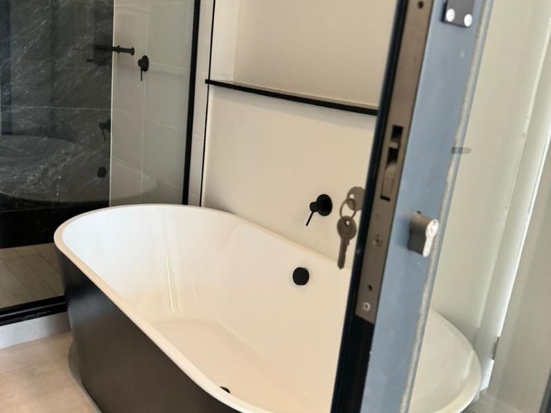 Modern bathroom featuring a sleek freestanding bathtub, walk-in shower with glass screen, and contemporary black matte fixtures.