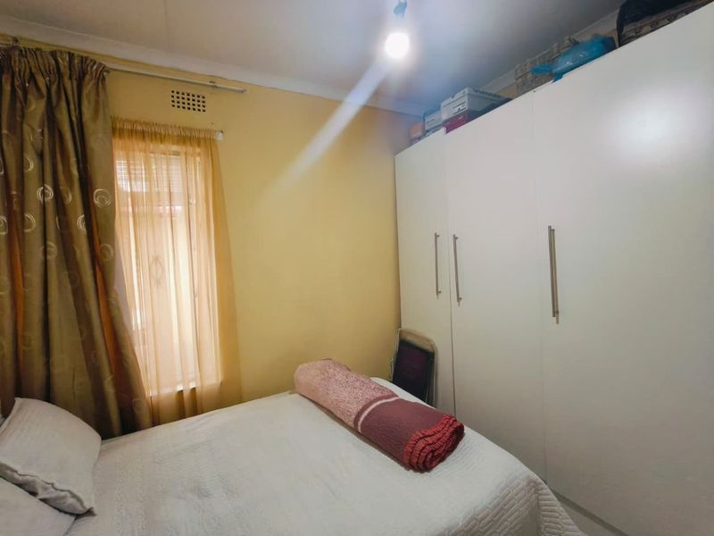 A functional bedroom featuring a large white built-in wardrobe and a window with curtain treatments.