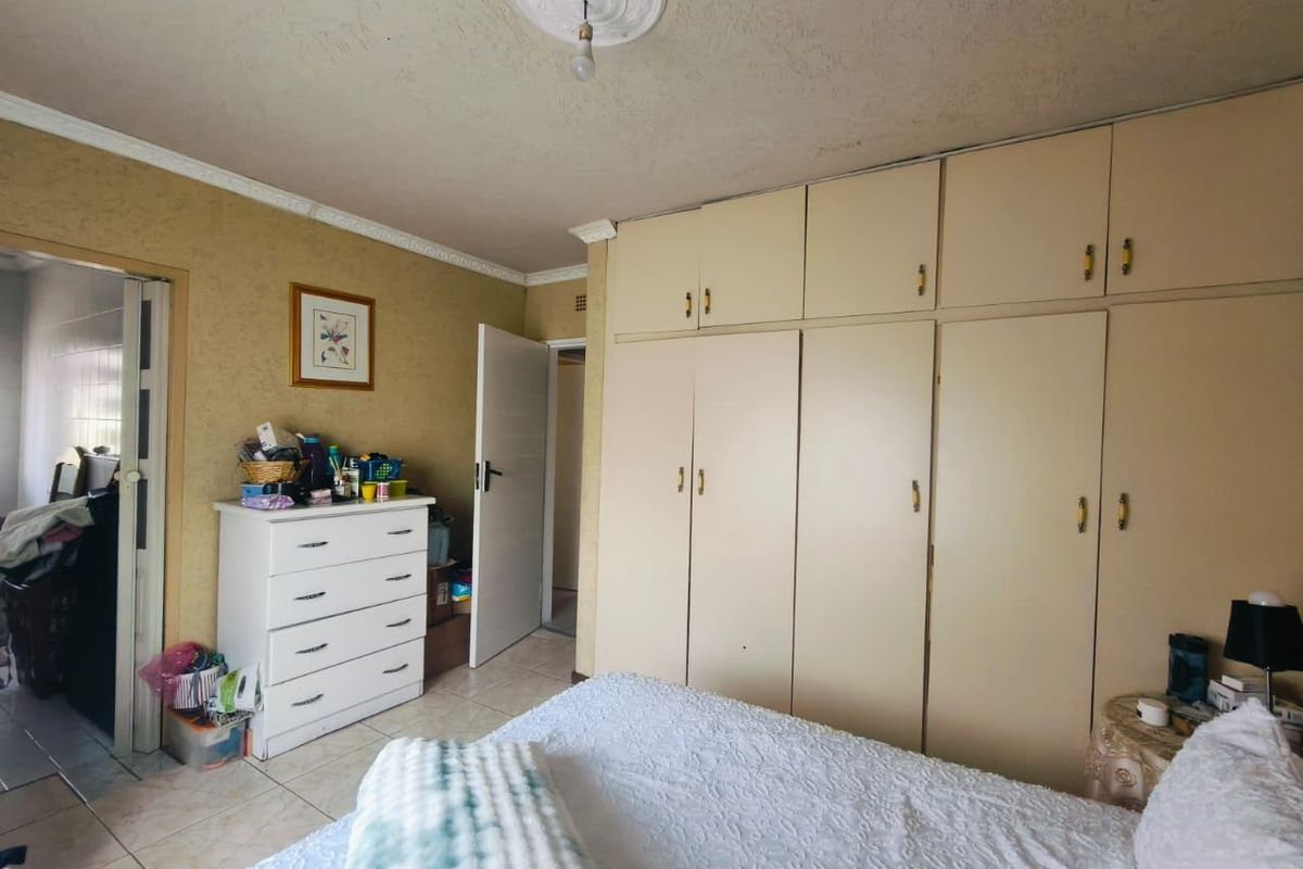 A bedroom featuring extensive built-in cupboards, tiled flooring, and decorative ceiling detailing. The space requires cosmetic updates to improve its overall condition.