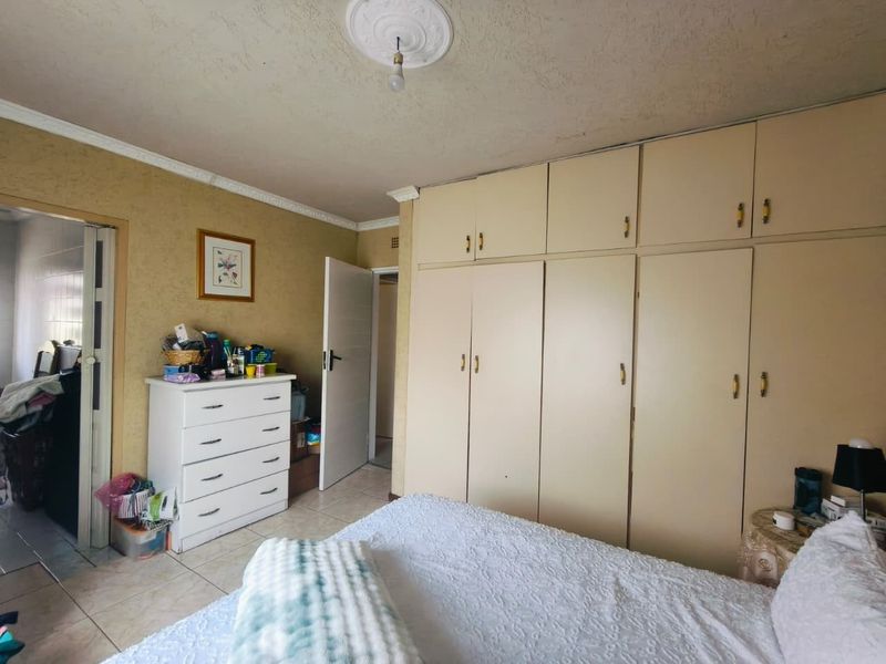 A bedroom featuring extensive built-in cupboards, tiled flooring, and decorative ceiling detailing. The space requires cosmetic updates to improve its overall condition.