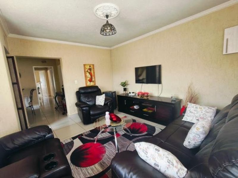A comfortable living room featuring tiled flooring, decorative ceiling rose, and coving, providing a functional space for relaxation and entertainment.