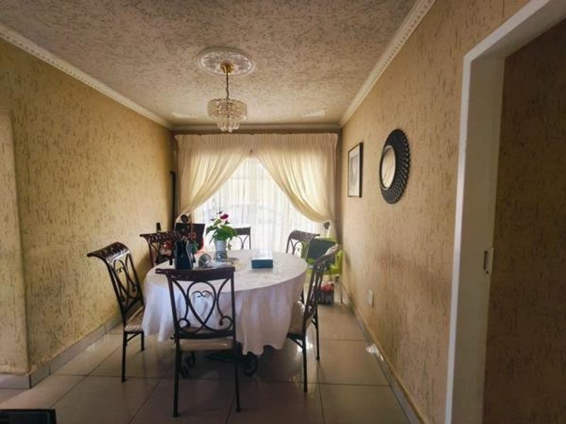 A dining room featuring tiled flooring, textured walls, and a central chandelier, providing a functional space for family meals.