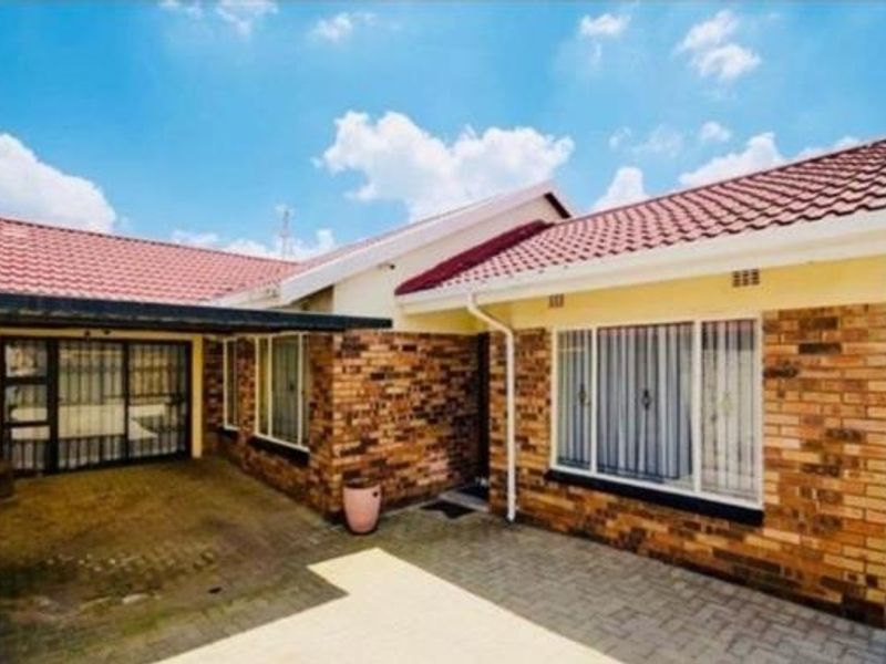 A well-maintained single-story face brick house featuring a tiled roof, paved driveway, and an integrated carport with secure window bars.