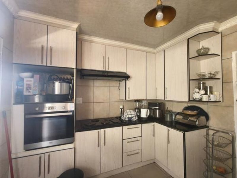 A functional kitchen featuring light wood-grain cabinetry, a built-in oven, electric hob, extractor fan, and tiled backsplash with practical open shelving.
