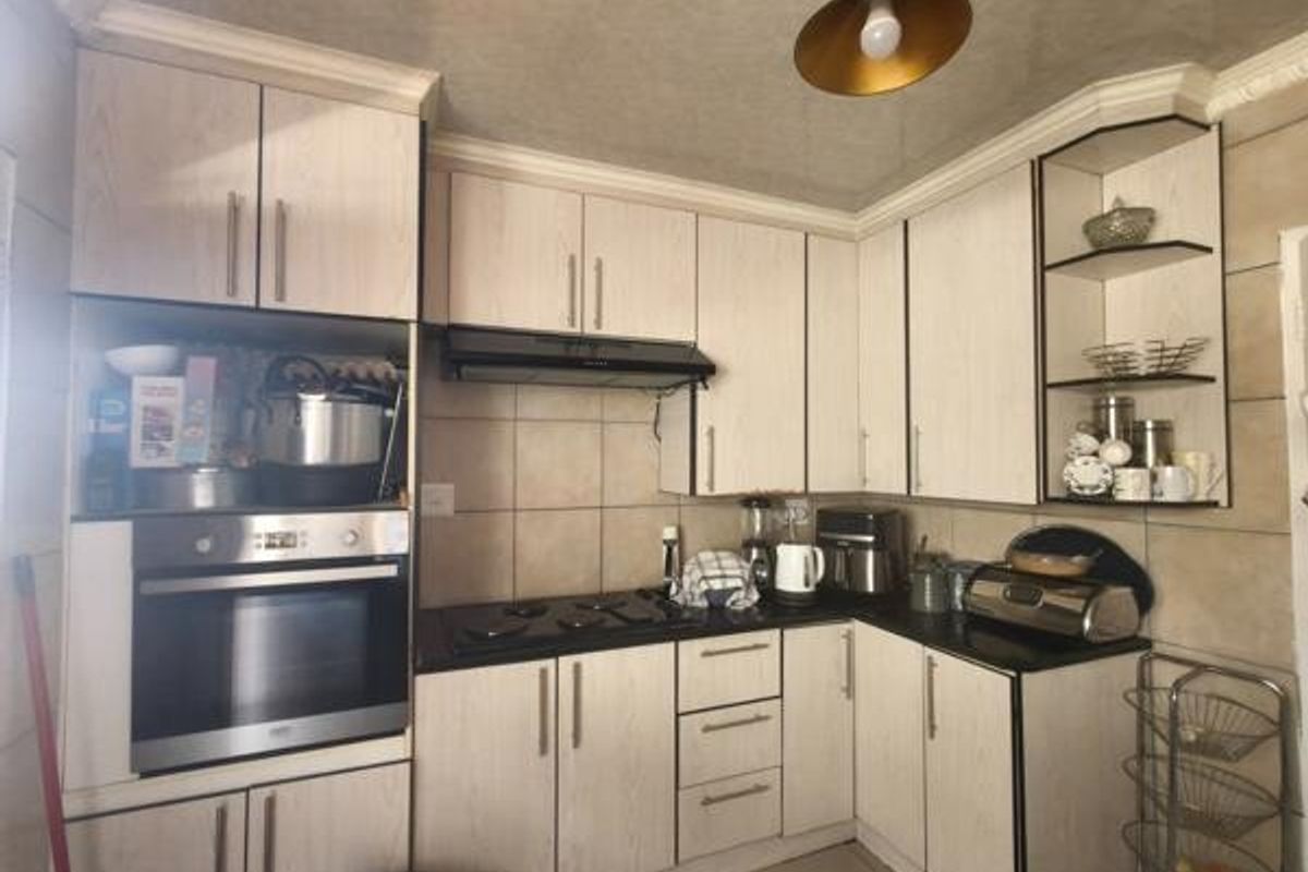A functional kitchen featuring light wood-grain cabinetry, a built-in oven, electric hob, extractor fan, and tiled backsplash with practical open shelving.