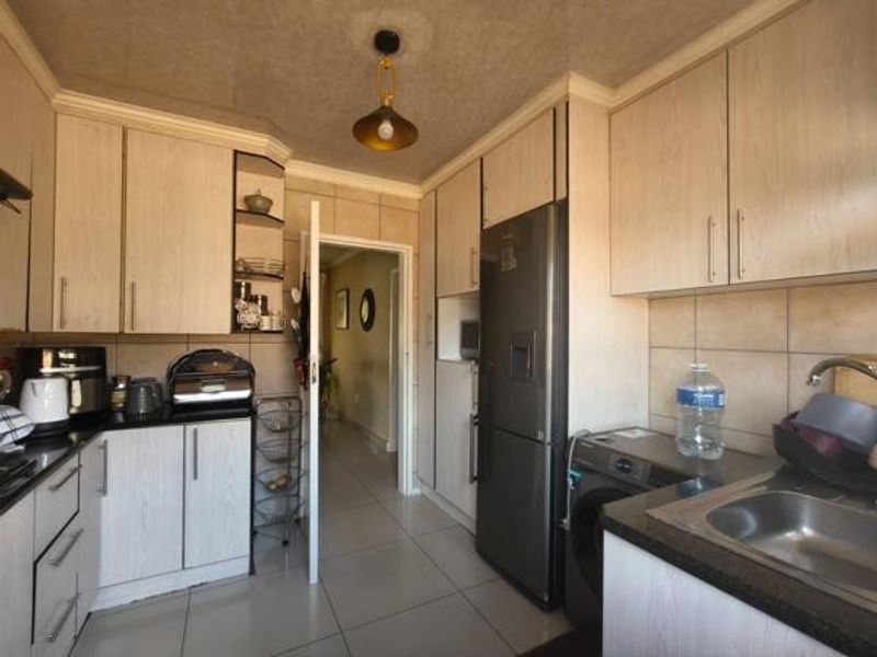A functional kitchen featuring light wood-grain cabinetry, dark countertops, tiled backsplash, and integrated space for appliances with direct access to the hallway.