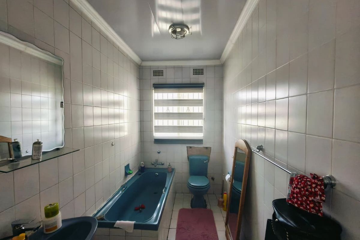 A functional bathroom featuring a blue bathtub, matching toilet and basin, fully tiled walls, and a window with security bars.