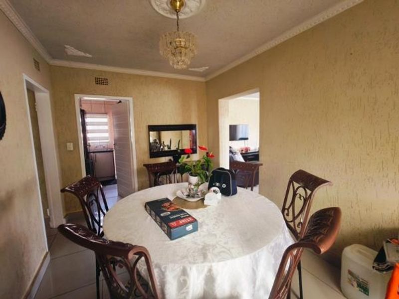 Dining room featuring tiled flooring, decorative ceiling rose with chandelier, and coving, providing a functional space with access to adjacent rooms.