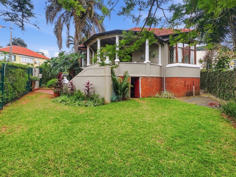 Rear view of a character home featuring a covered veranda, brick foundation, and established garden surroundings.