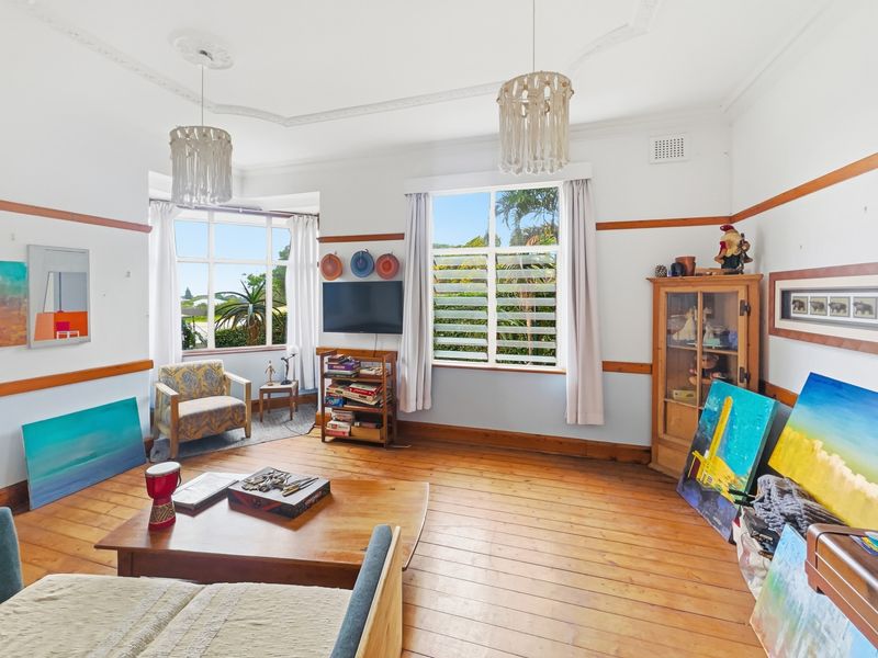 A bright living room featuring original timber flooring, decorative ceiling roses, picture rails, and large windows providing natural light and garden views.