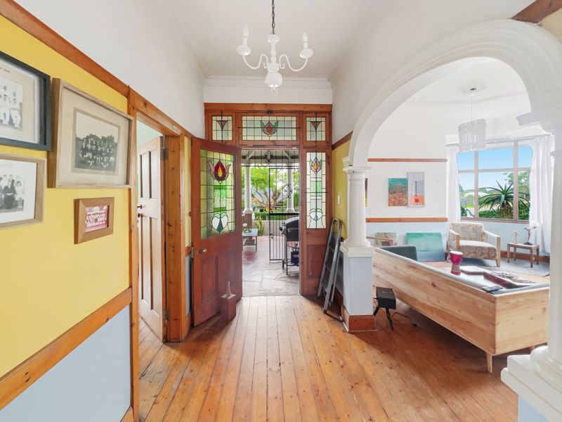A character-filled hallway featuring original timber flooring, decorative archways, and a beautiful stained glass entrance door leading to an outdoor patio area.