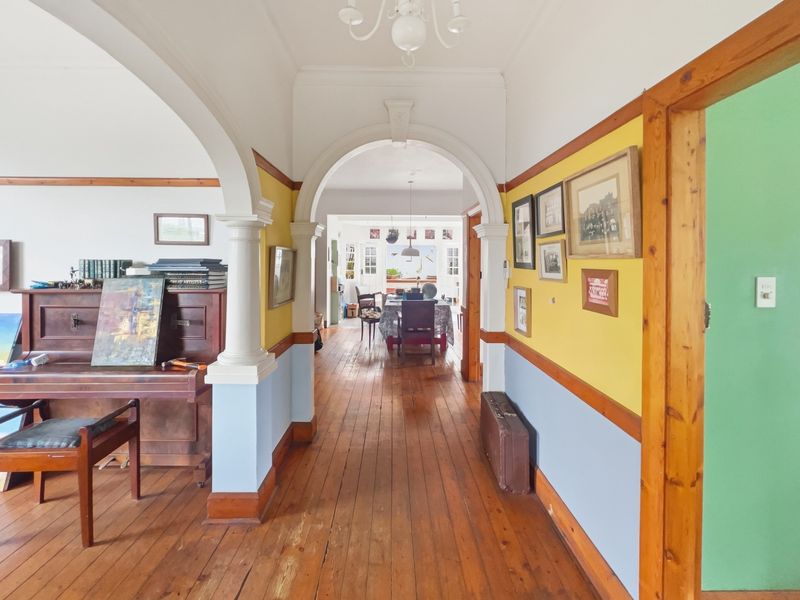 A character-filled hallway featuring original hardwood flooring, decorative archways with columns, and classic timber door frames, connecting the main living areas.