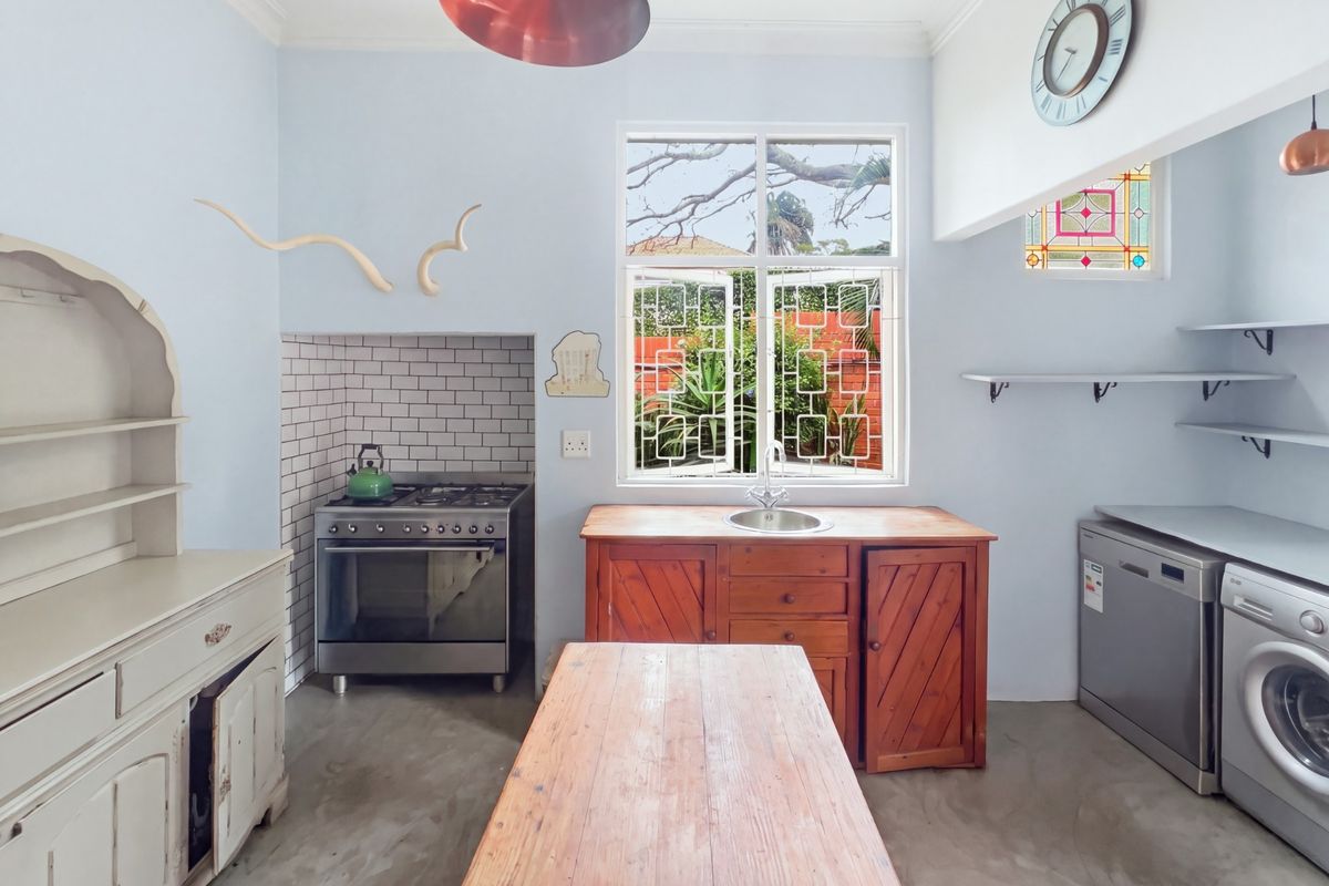 A characterful kitchen featuring a gas stove with subway tile backsplash, wooden cabinetry, stainless steel sink, and unique stained glass accents.