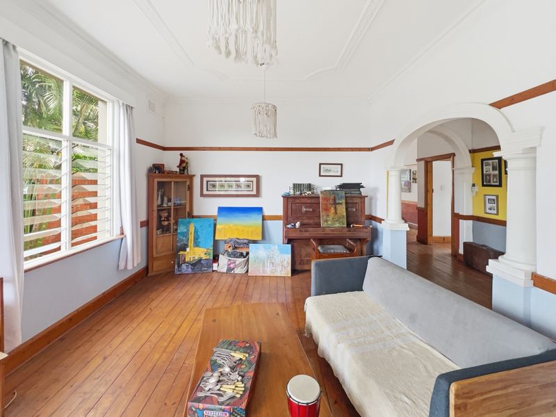 A character-filled living room featuring original timber flooring, decorative ceiling details, and a classic archway leading to the hallway.