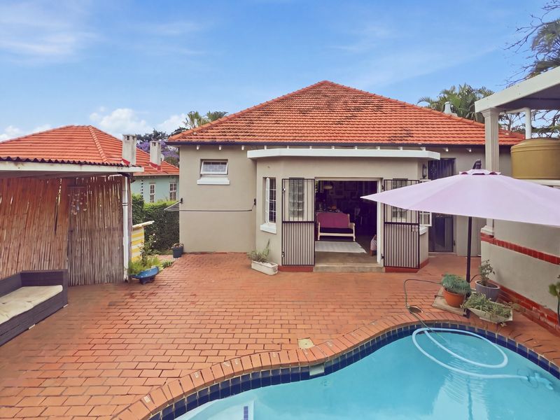 Rear exterior view featuring a swimming pool, brick paved patio area, and a covered gazebo, providing a functional outdoor entertainment space.