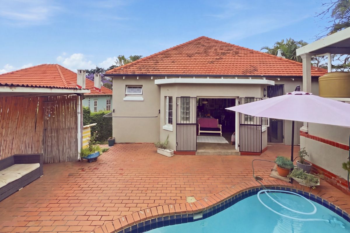 Rear exterior view featuring a swimming pool, brick paved patio area, and a covered gazebo, providing a functional outdoor entertainment space.