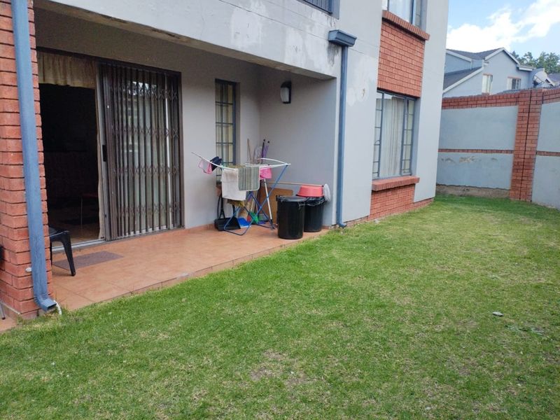 Rear view of the apartment featuring a tiled patio, sliding security gate, and a private lawn area with boundary walling.