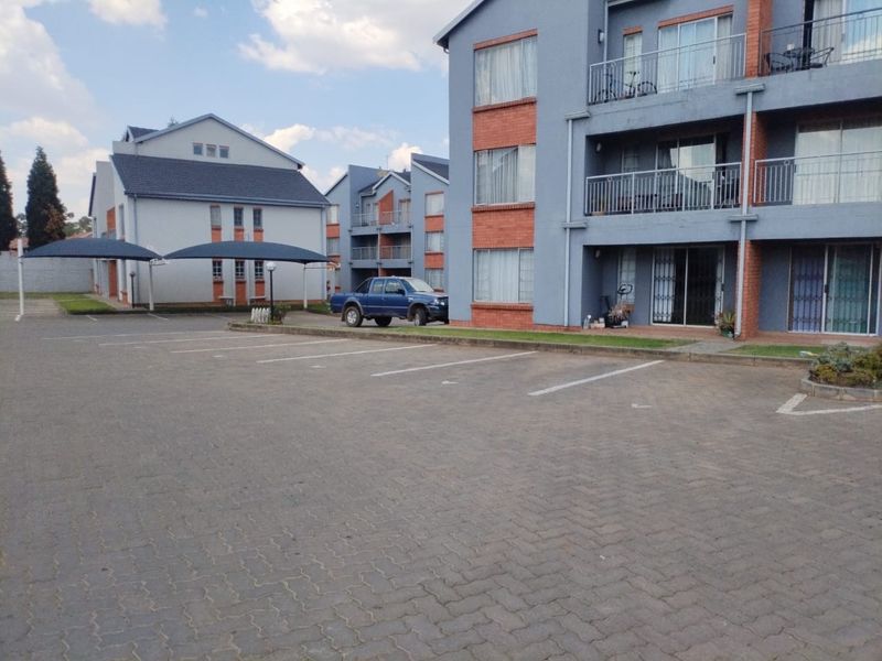 Exterior view of a multi-story apartment complex featuring paved parking, covered parking bays, and private balconies with sliding door access.