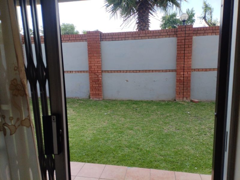 A private rear garden featuring a tiled patio area and a secure brick boundary wall, accessible via a sliding security gate.