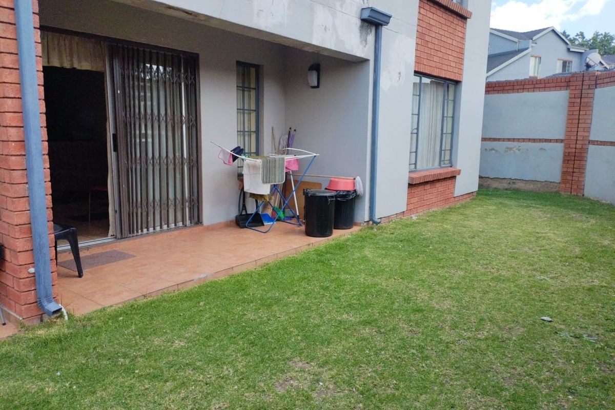 Rear view of the apartment featuring a tiled patio, sliding security gate, and a private lawn area with boundary walling.