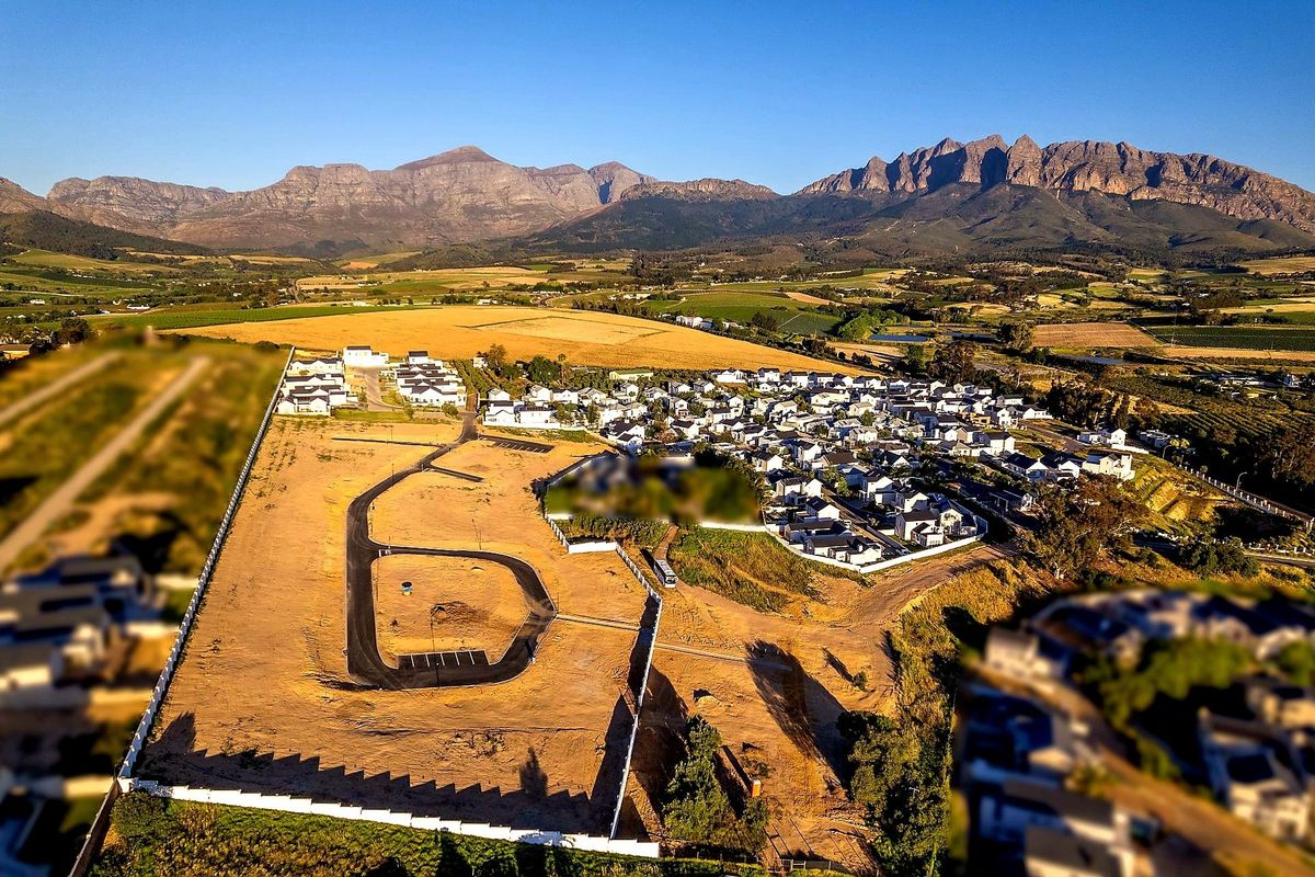 Aerial view of a residential development site featuring a paved internal road, perimeter fencing, and surrounding mountain landscape.