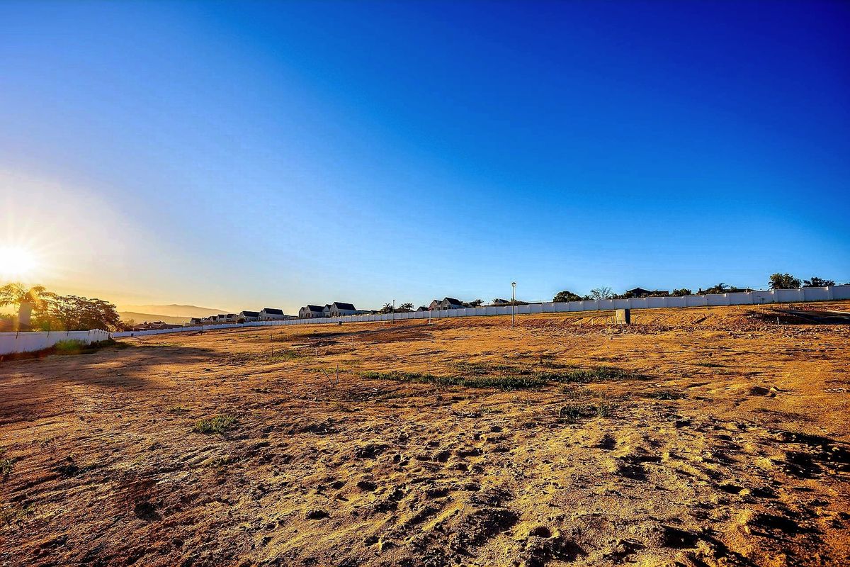 A wide-angle view of a vacant residential plot featuring a perimeter wall and clear horizon, ideal for new construction.