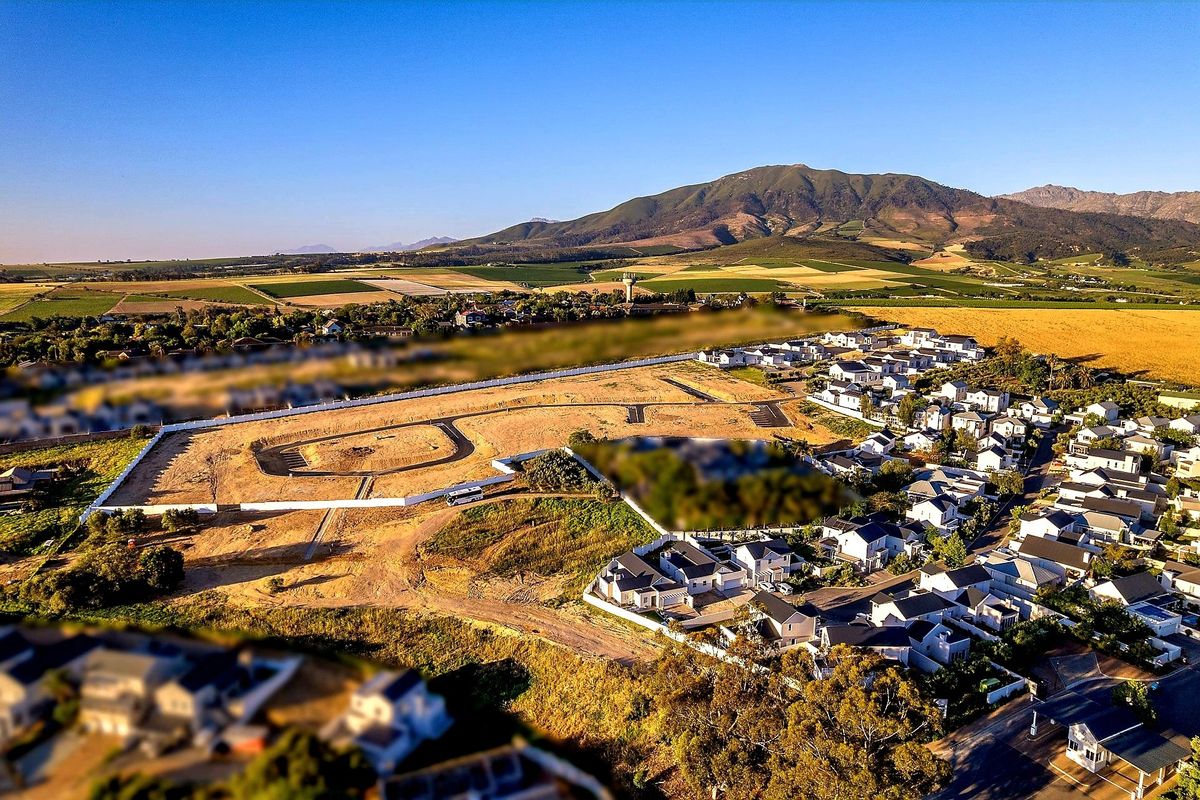 Aerial view of a residential development site featuring paved roads and perimeter fencing, set against a scenic mountain landscape.