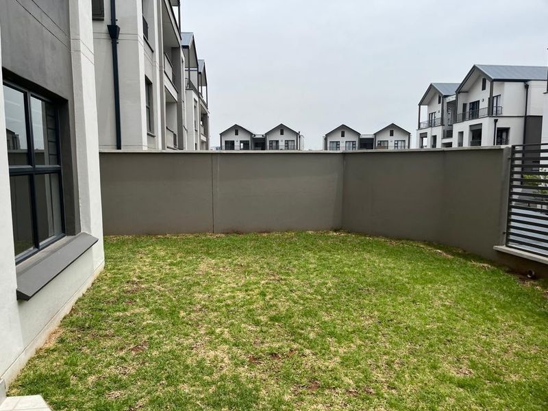 A private rear garden area featuring a well-maintained lawn enclosed by a solid boundary wall and modern apartment building architecture.