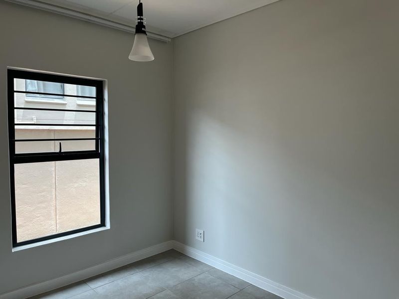 A clean, empty bedroom featuring neutral walls, tiled flooring, and a modern black-framed window, providing a blank canvas for personalization.