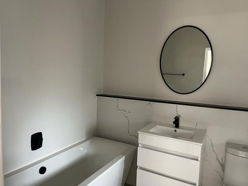 Modern bathroom featuring a sleek built-in bathtub, vanity with integrated sink, and elegant marble-look wall tiles with black accent finishes.