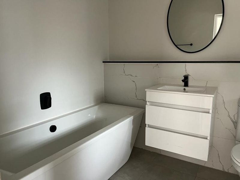 Modern bathroom featuring a sleek freestanding bathtub, wall-mounted vanity with black matte tapware, and elegant marble-look wall tiling.