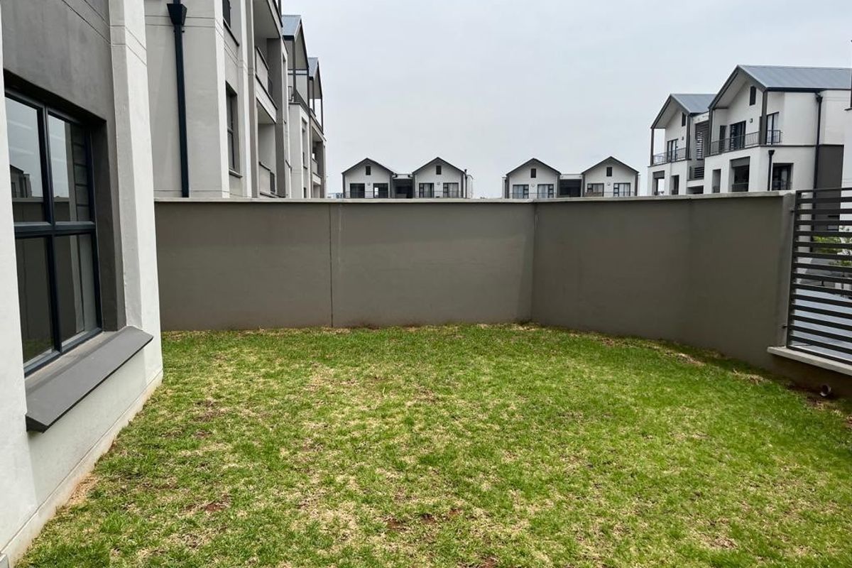 A private rear garden area featuring a well-maintained lawn enclosed by a solid boundary wall and modern apartment building architecture.