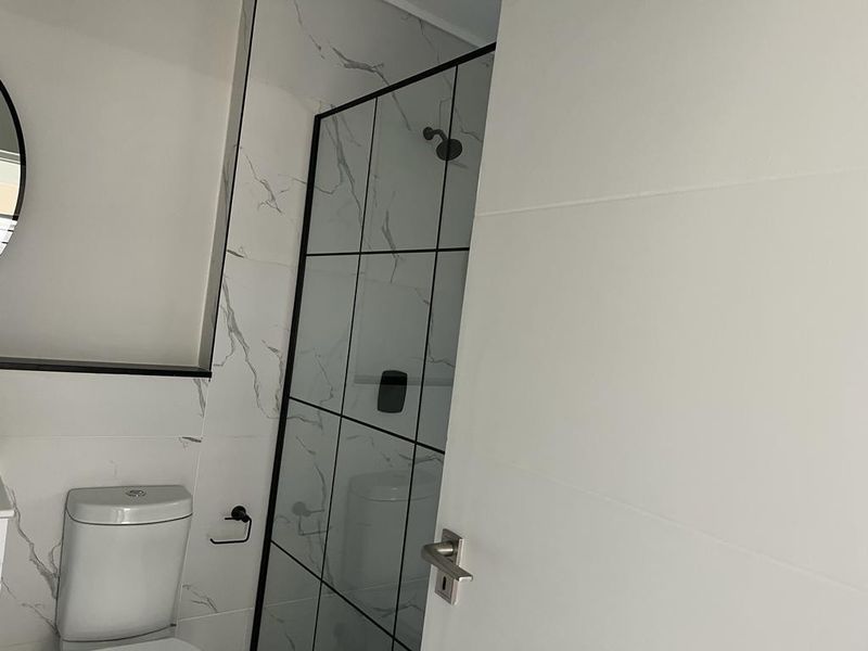Modern bathroom featuring marble-look wall tiles, a sleek black-framed shower enclosure, and a contemporary toilet.