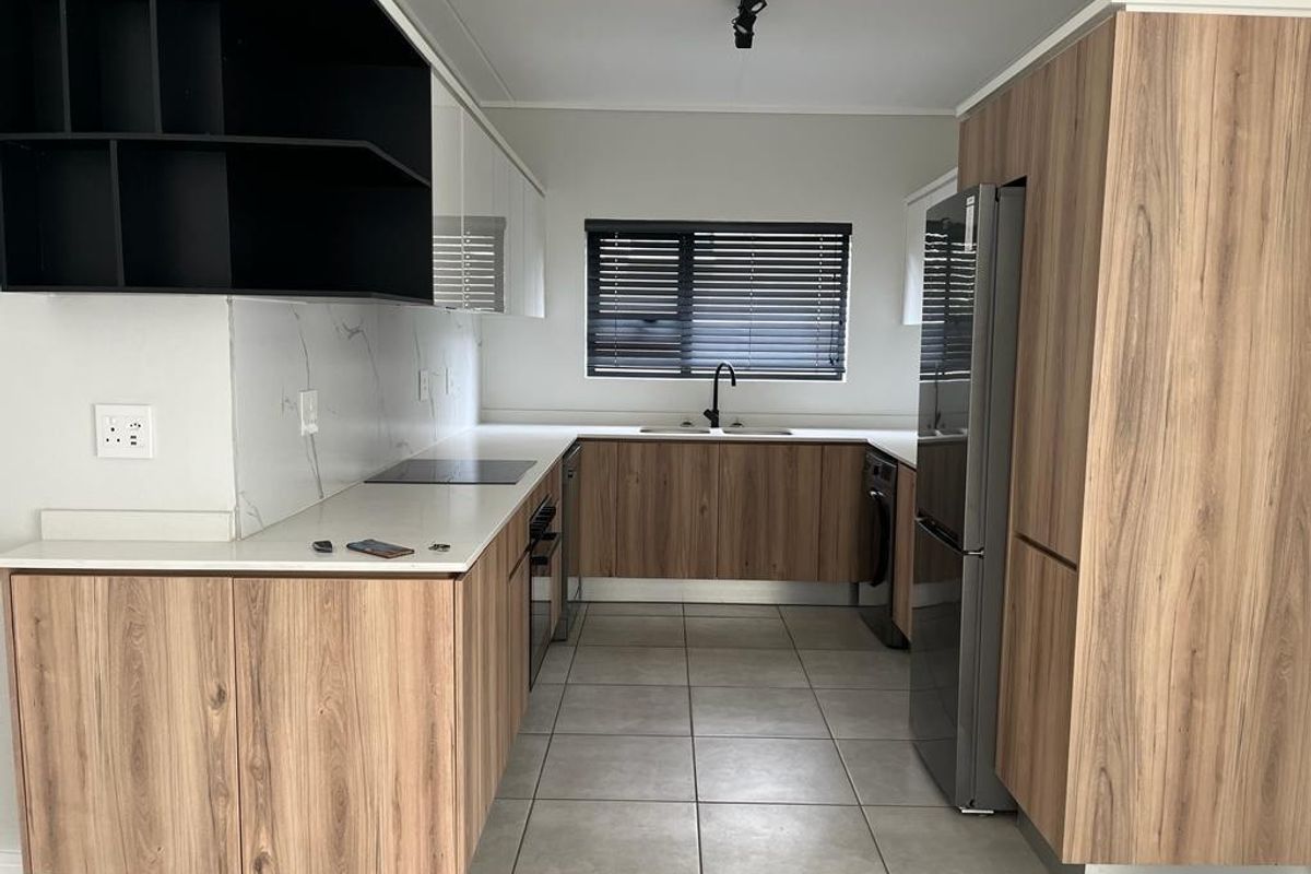 Modern kitchen featuring wood-grain cabinetry, stone countertops, marble-look splashback, integrated appliances, and tiled flooring in a clean, contemporary layout.