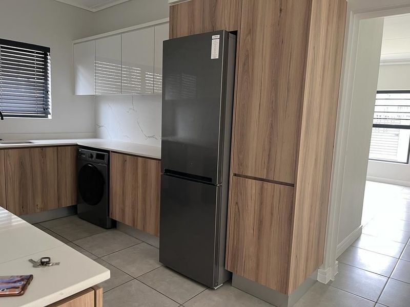 Modern kitchen featuring wood-grain and white cabinetry, stone countertops, marble-look splashback, and integrated laundry appliances in a clean, contemporary layout.