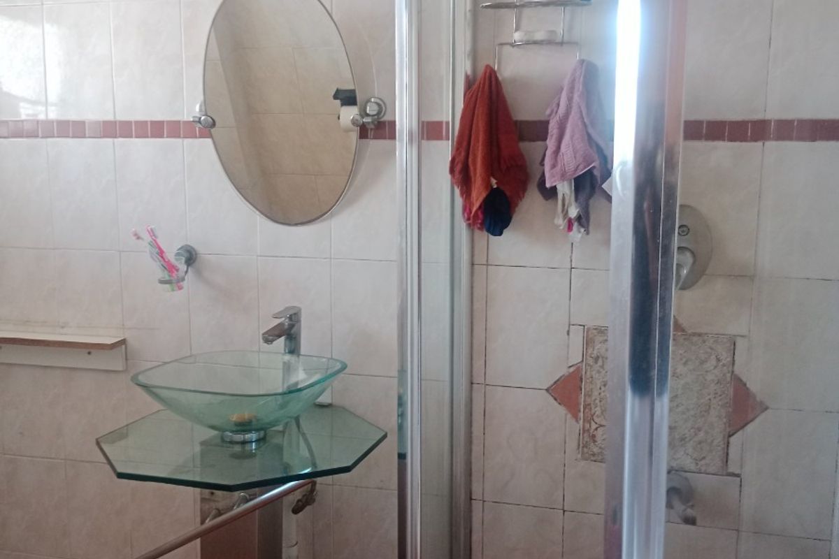 A bathroom featuring a glass vessel sink, pedestal vanity, and a shower enclosure with tiled walls. The space shows signs of wear and requires maintenance.