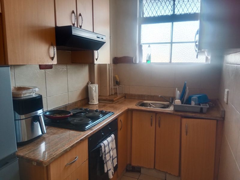 A compact kitchen featuring wooden cabinetry, laminate countertops, a built-in oven, and an electric hob, requiring cosmetic updates to modernize the space.
