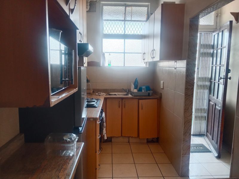 A compact kitchen featuring built-in wooden cabinetry, laminate countertops, a stainless steel sink, and a hob, with direct access to an exterior security gate.