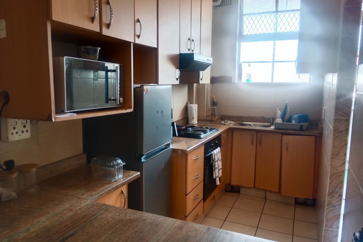 A functional kitchen featuring laminate cabinetry, built-in oven, hob, extractor fan, and tiled finishes, offering a practical layout for daily meal preparation.