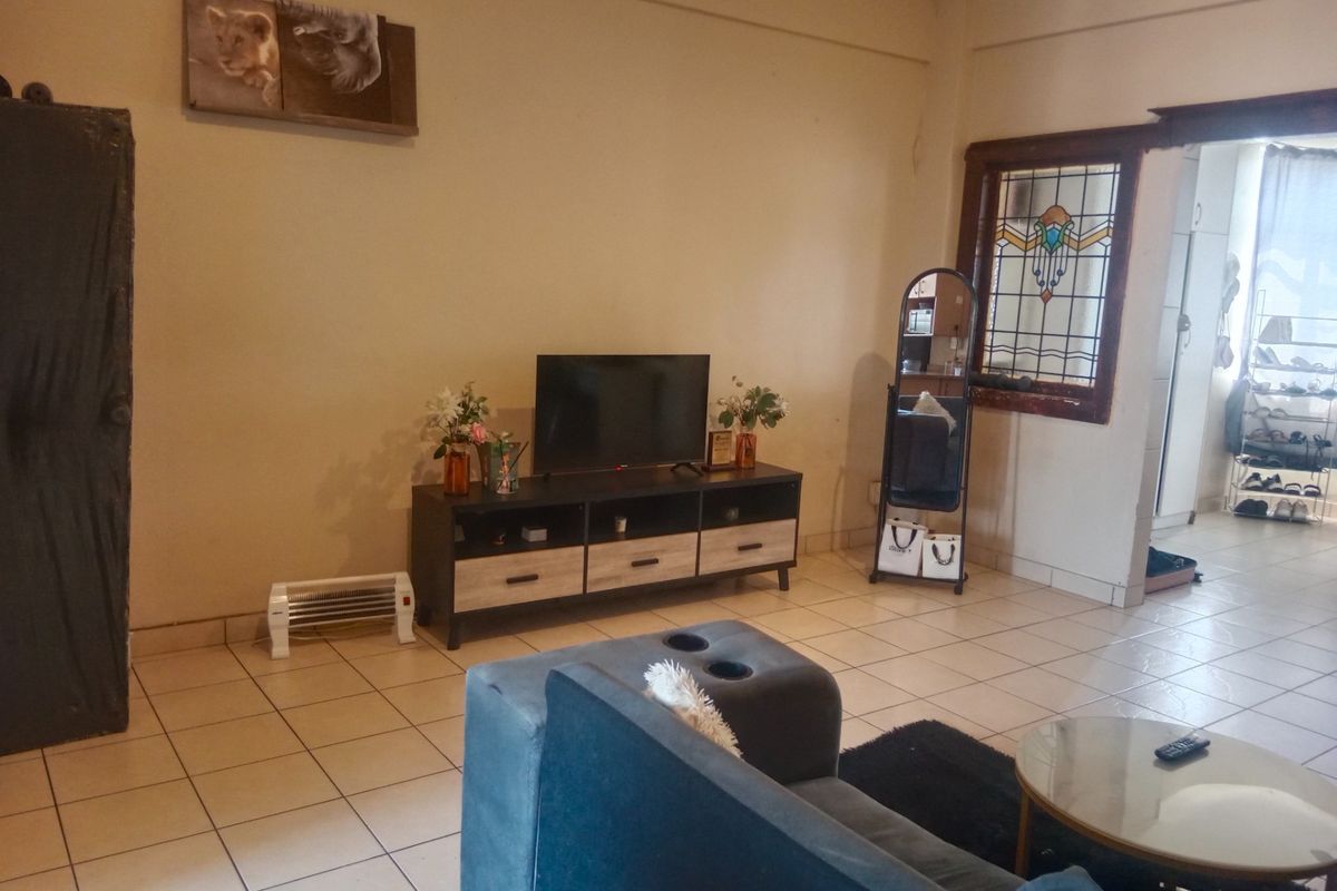 A living room featuring tiled flooring and a decorative stained glass window, showing signs of wear on the walls and window frame.