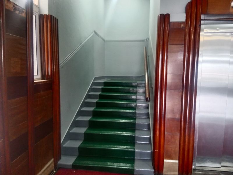 A communal apartment hallway featuring a staircase with a handrail, wood-paneled walls, and an elevator access point.